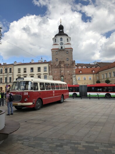 Na tle Bramy Krakowskiej stoi stary czerwony autobus marki Jelcz.