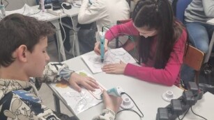 Uczniowie klasy 5c siedzą przy stolikach i wykonują prace używając długopisów 3D.