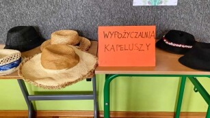 Opis zdjęcia : Sześć kapeluszy leży na ławce szkolnej, obok stoi kartka „Wypożyczalnia kapeluszy”