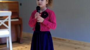 Dziewczynka stoi na scenie, trzyma w ręce mikrofon, patrzy przed siebie.