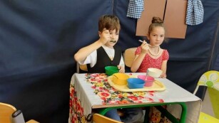 Scena z przedstawienia-chłopiec i dziewczynka udają, że jedzą zupę.